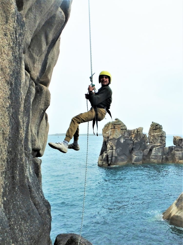 Young rock climber abseiling down a sheer cliff with Kernow Coasteering on a beginner rock climbing course in Cornwall