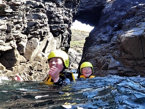 Two young people go through a sea arch in Cornwall on a beginner coasteering trip at Praa Sands with Kernow Coasteering