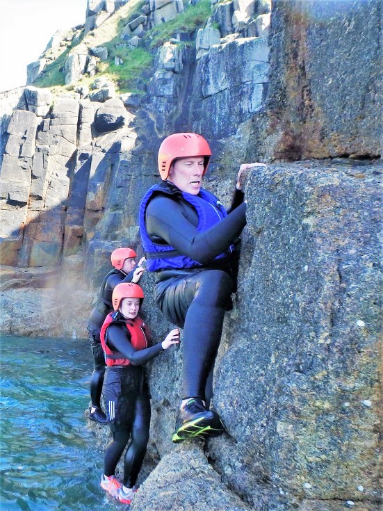 Coasteering group traversing over steep rock at Land's End in Cornwall