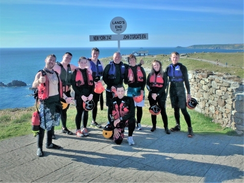 Coasteering group at Land's End landmark signpost having completed Cornwall's ultimate coasteering adventure with Kernow Coastee