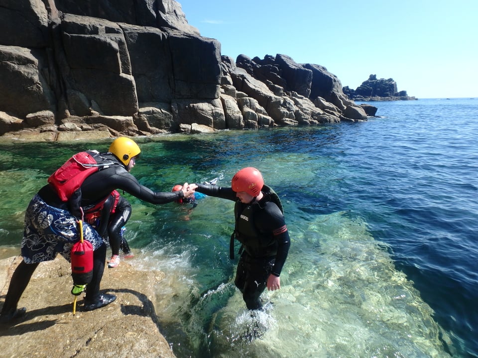 Coasteering at Land;s End in Cornwall, a coasteering instructor is helping a group member exit the water
