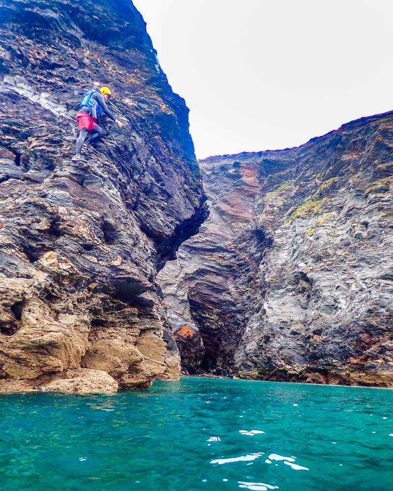 Coasteering Explorer high on a rock face, Deep Water Soloing int Zawn Shagg, Porthleven, Cornwall