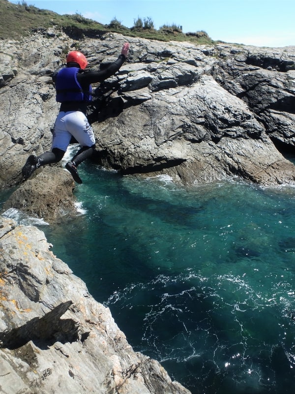 Coasteering at Prussia Cove, near Penzance, Cornwall. Here coasteerer does a large jump into crystal blue waters.