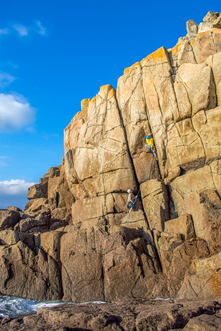 Climber climbs golden granite cliffs at Carn Boel, near Land's End Cornwall