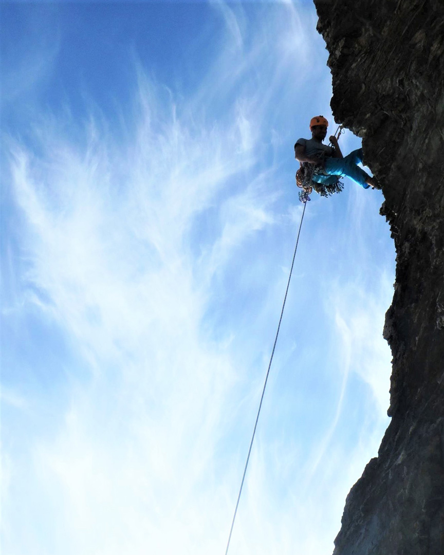 Climber Abseiling down a cliff in Cornwall, silhouette with whispy clouds in the sky