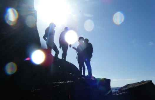 Coasteering at Land's End. Here a coasteering group is silhouetted in the Cornish sun.
