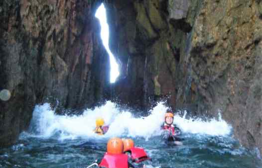 Group getting washed through an archway by a wave coasteering in Cornwall with Kernow Coasteering