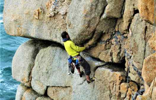 Rock climber on the crux of Demo Route at Sennen, Cornwall