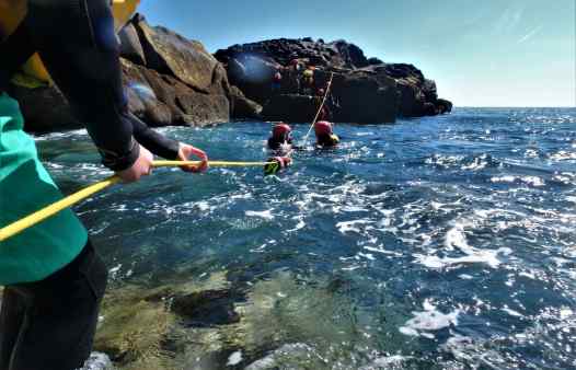 Coasteering guides set up a rope to help group cross rough sea on the Isles of Scilly