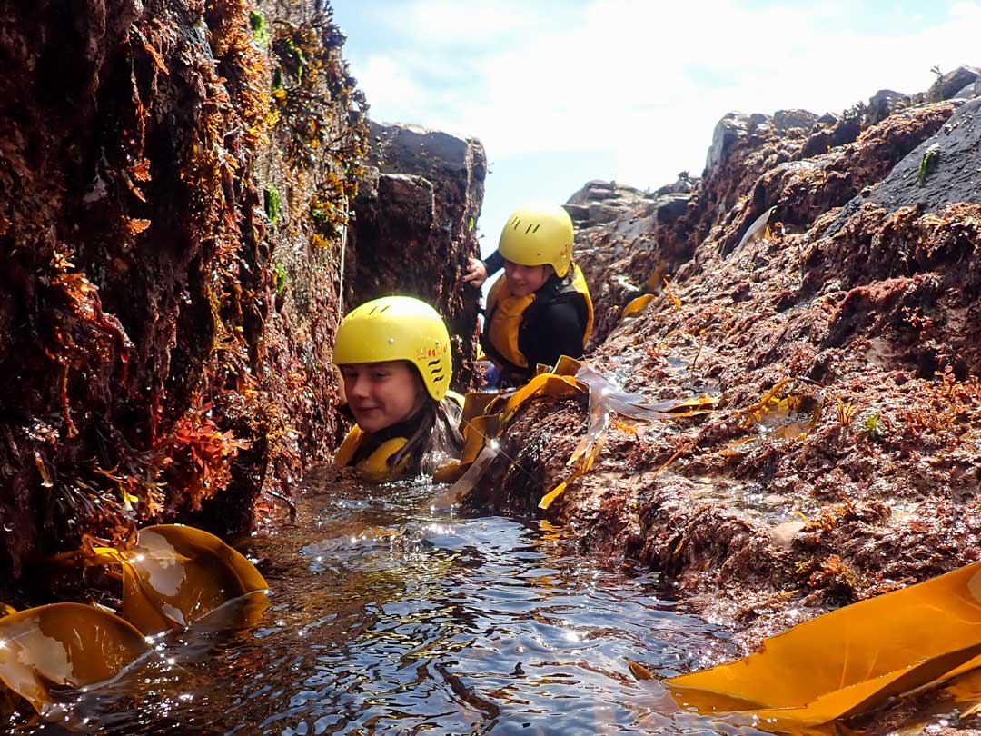 Coasteerers exploring narrow gullies at low tide at Praa Sands