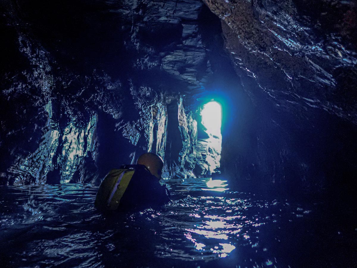 Coasteering explorer navigating a vast sea cave near Godrevy, Cornwall, where a torch would be essential
