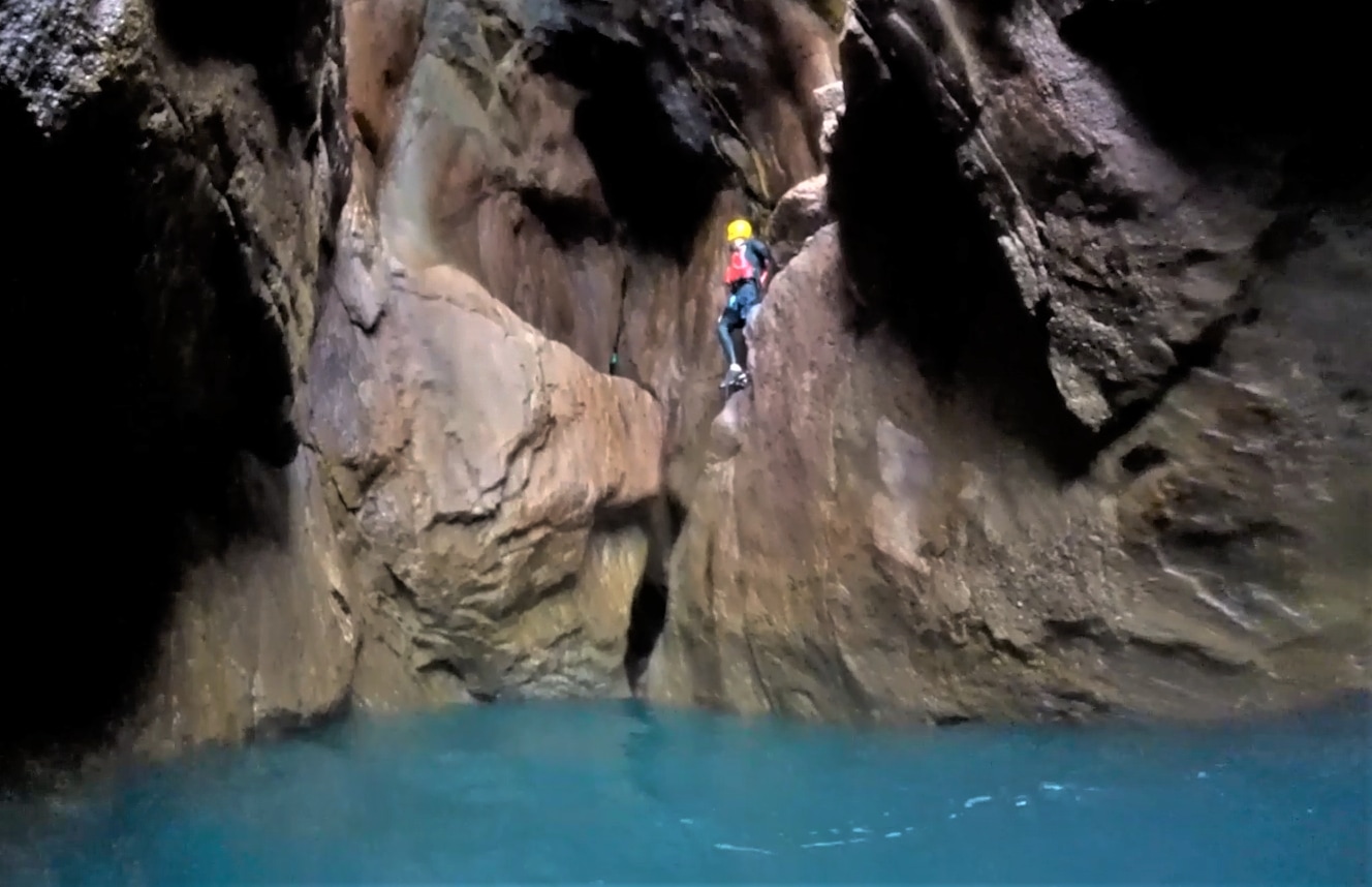 Coasteerer climbing along the wall inside the third sea cave at Trevean Cliff near Porthcurno, Cornwall.