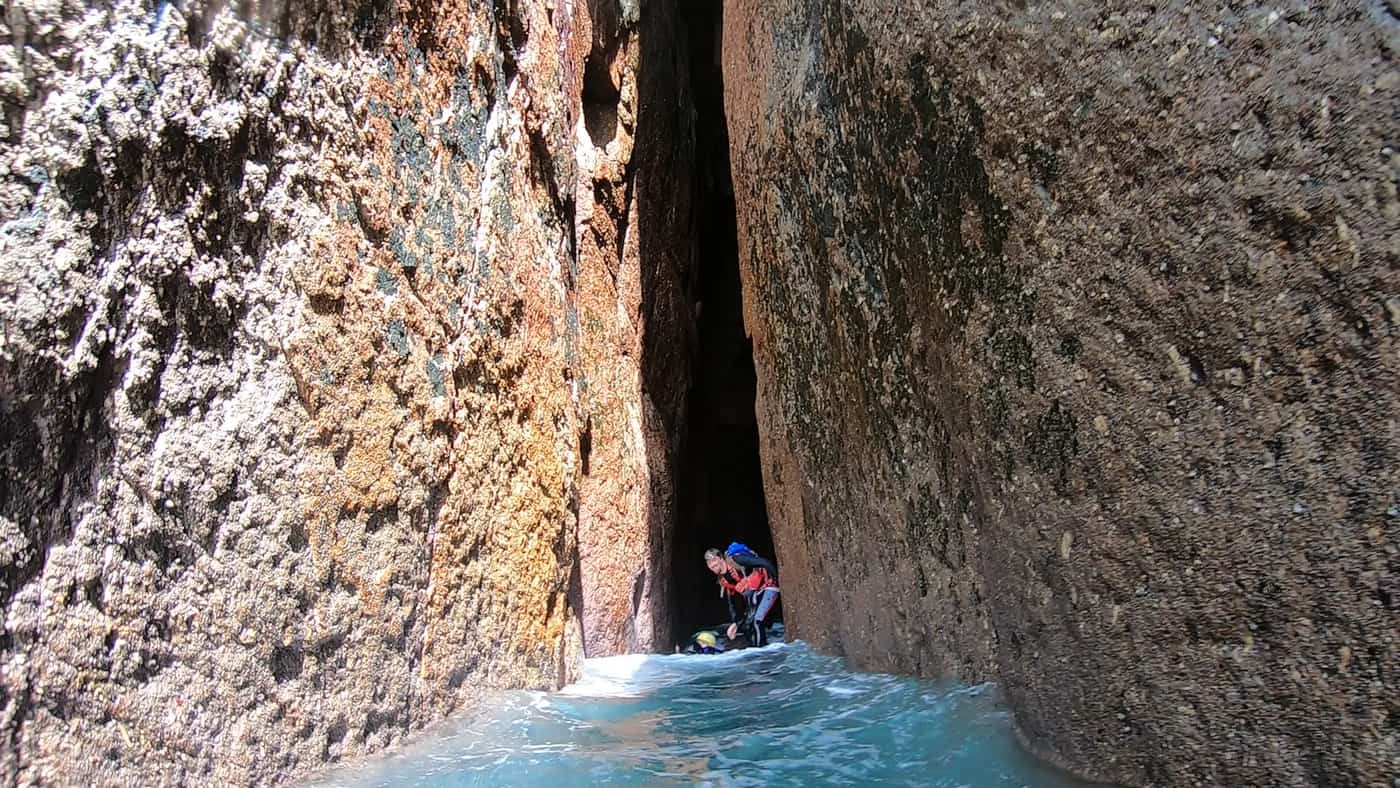 Coasteering guide entering a narrow coastal cave at Carn Barra on Cornwall’s granite coast.