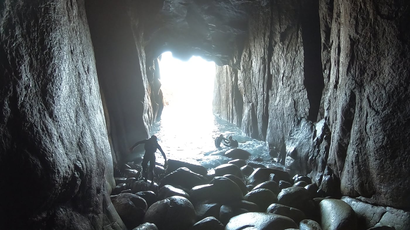 Coasteering inside the main sea cave at Carn Barra in west Cornwall, looking out toward the bright entrance.