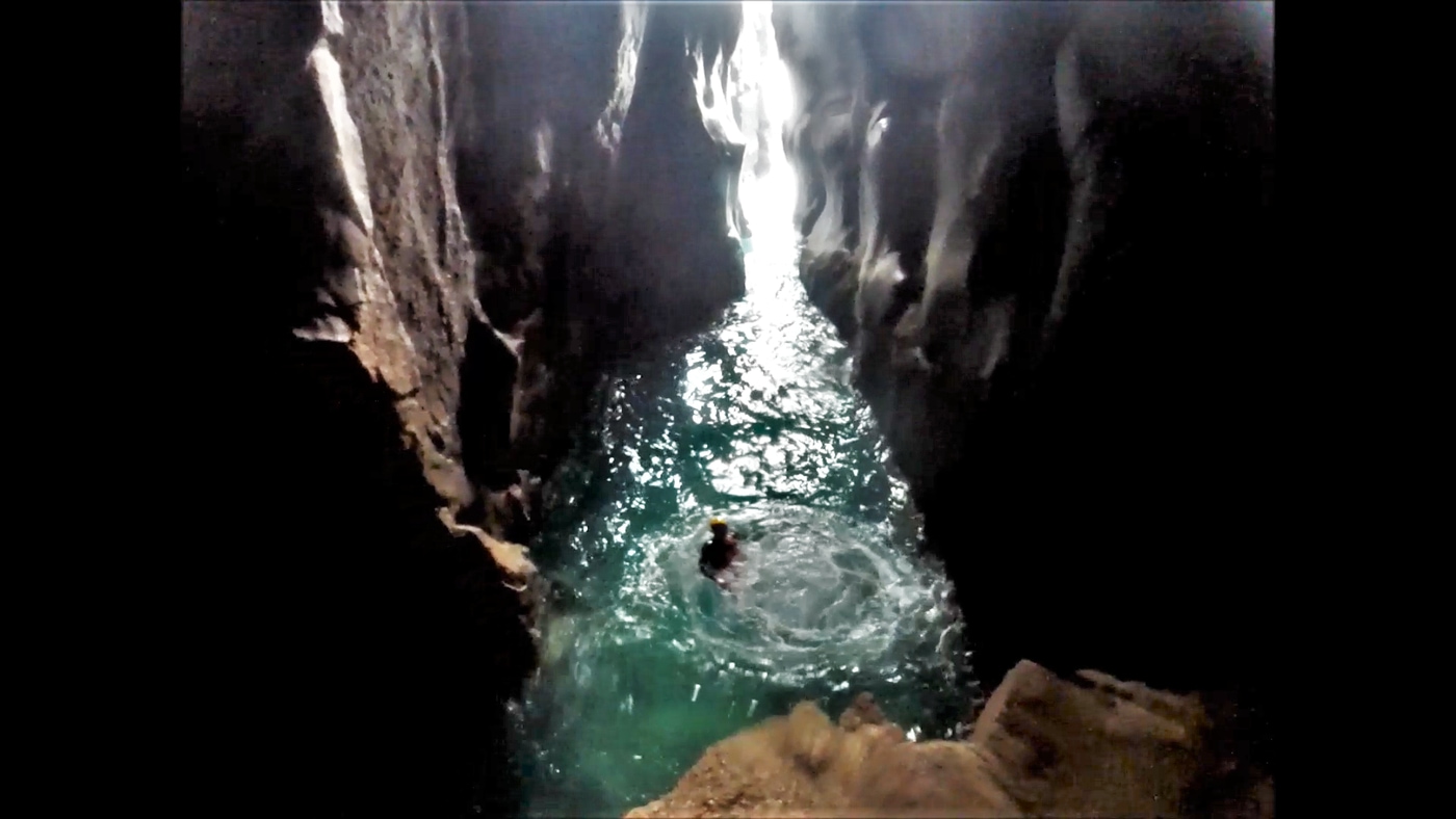 Person coasteering into the main sea cave at Trevean Cliff near Porthcurno in west Cornwall, surrounded by towering rock walls.