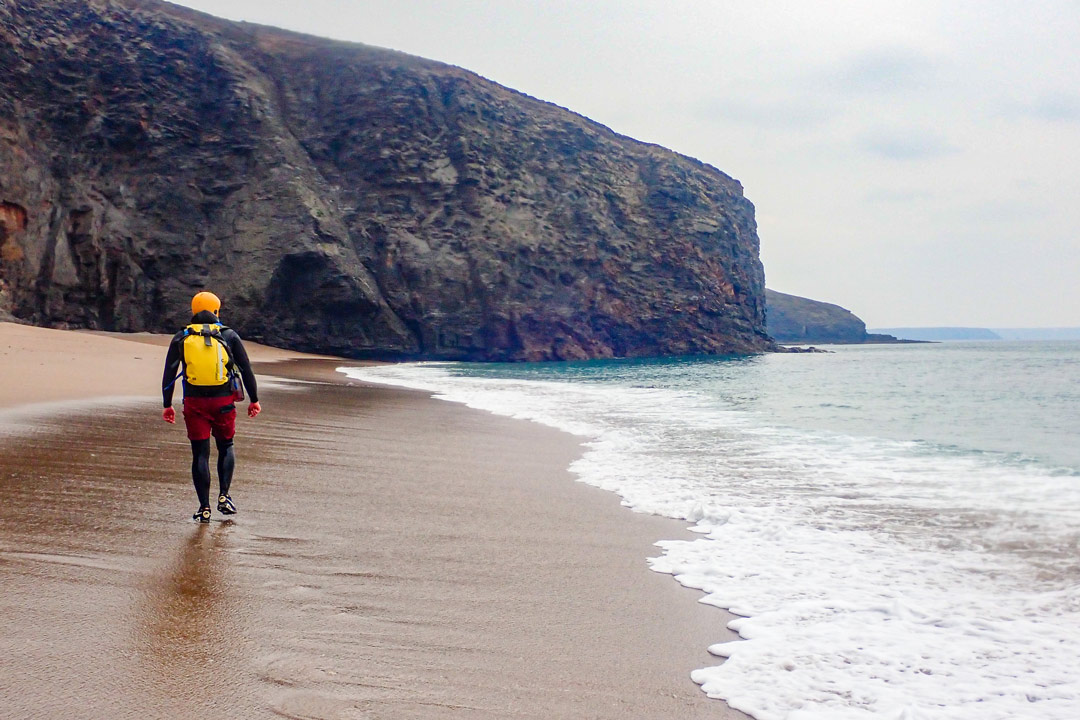 Coasteering explorer with waterproof rucksack at remote cove near Porthleven, Cornwall