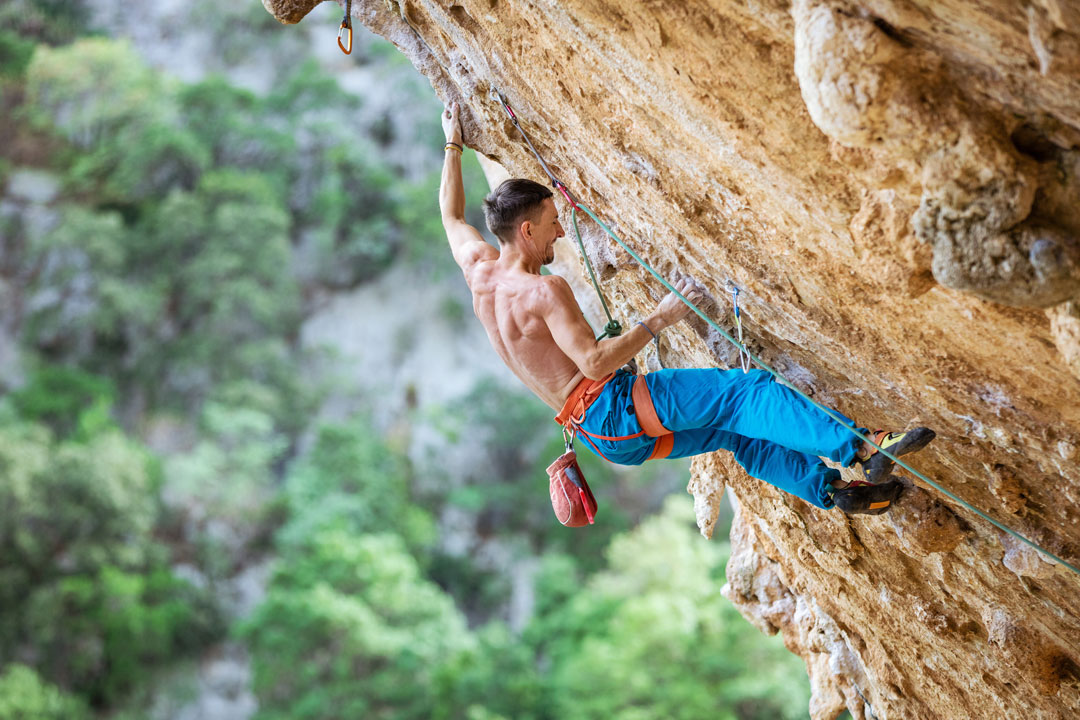 Male sport climber wearing rock climbing shoes on a steep limestone route in Kalymnos, Greece