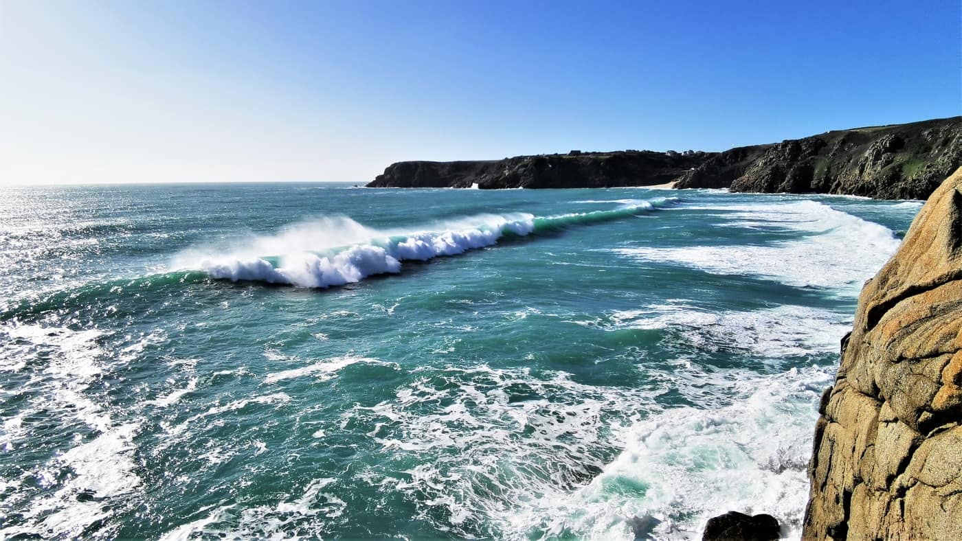 Powerful Atlantic waves breaking in Porthcurno Bay, shaping the sea caves in Cornwall.