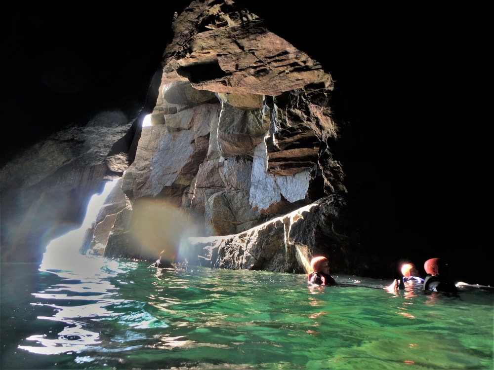 Coasteering group swimming out of the Great Cave at Land’s End, one of the most spectacular sea caves in Cornwall.