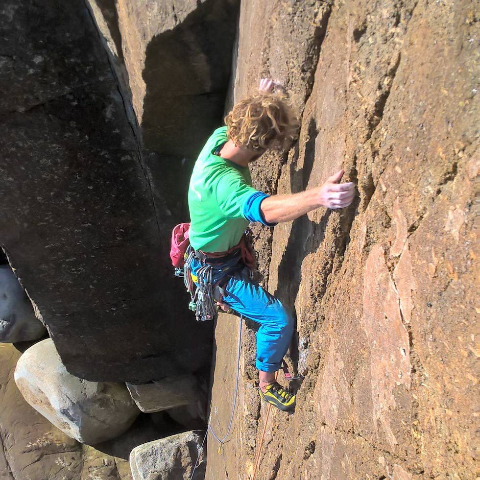 Climber placing micro wires on the granite face of Grand Plage (E3) at Carn Barra – showcasing micro trad gear placement on small cracks.