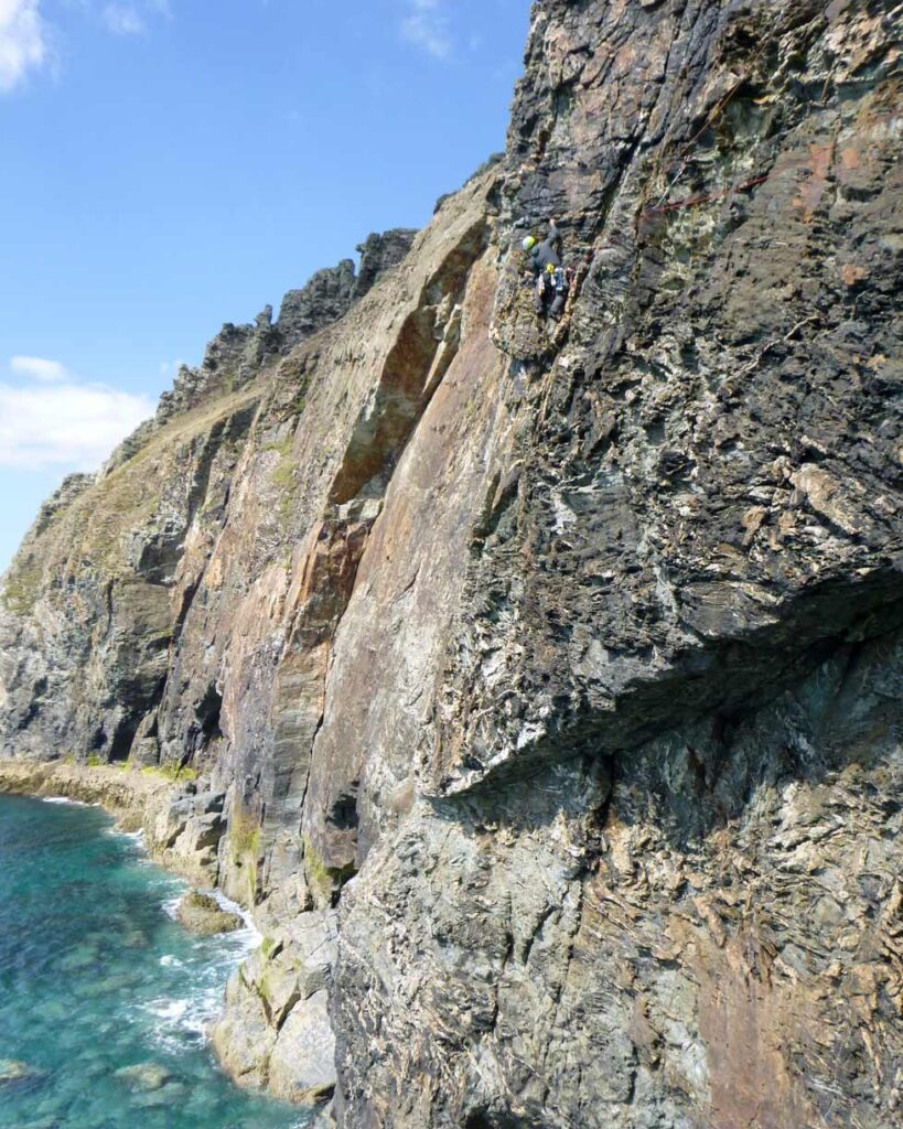 Trad climber leading Journey to Ixtlan at Carn Gowla, using slings to protect multiple threads on the sea cliff.