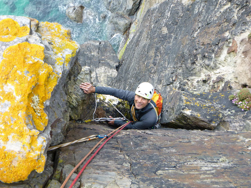 Climber seconding and cleaning gear on a steep sea cliff trad climbing route.
