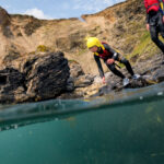 Young coasteerer preparing to leap into the sea on a beginner coasteering adventure at Praa Sands.