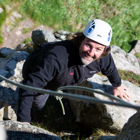 Beginner climber smiling as they take part in an outdoor climbing Cornwall experience for first-timers