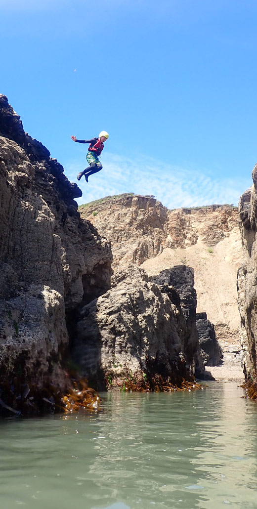 Young person launching from one of the highest jumps on the beginner coasteering session in Cornwall