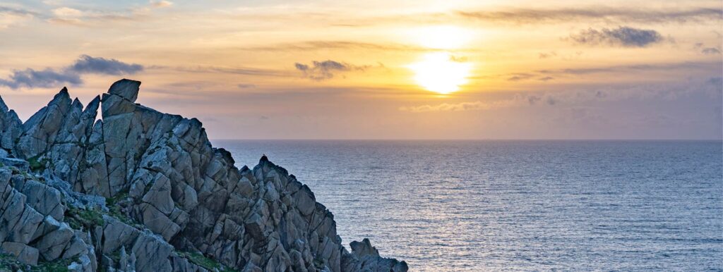 A golden sunset over the jagged granite pinnacles of Commando Ridge at Bosigran, west Cornwall, with the Atlantic Ocean beyond