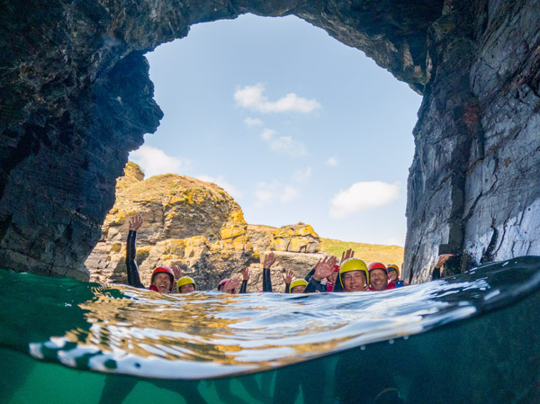 Group exploring a sea cave and floating in the water during a coast steering adventure along the dramatic Cornwall coastline – a perfect example of the adventure activities Cornwall offers visitors.