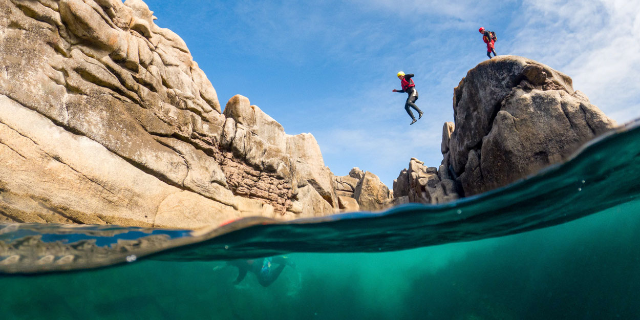 Person leaping from granite cliffs into clear water on a coasteering adventure – perfect for those exploring the adventure activities Cornwall has to offer and wondering what to do in Cornwall and the Isles of Scilly