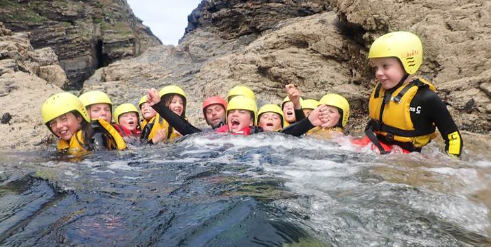 Group of children laughing and relaxing in a natural pool during a coasteering session in Cornwall