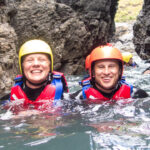 Smiling couple wade through a narrow sea gully on a child-friendly coasteering session in Cornwall