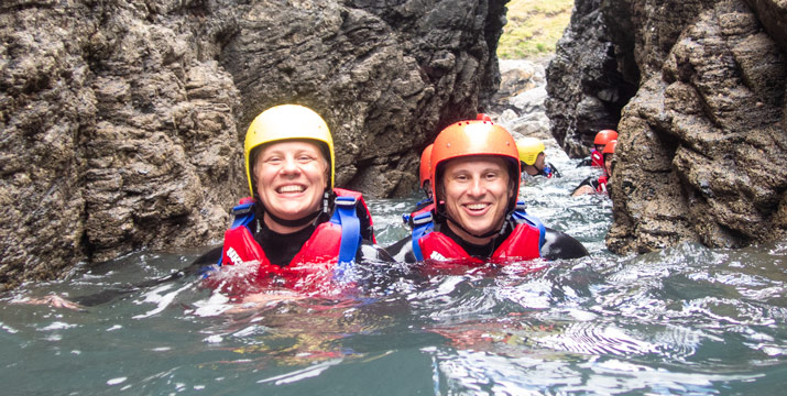 Smiling couple wade through a narrow sea gully on a child-friendly coasteering session in Cornwall