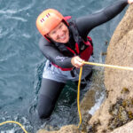 Woman using a fixed throwline to climb out of the sea during coasteering in Cornwall