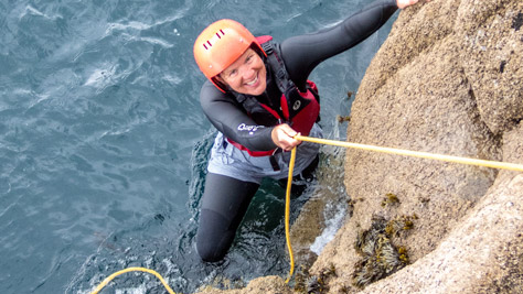Woman using a fixed throwline to climb out of the sea during coasteering in Cornwall