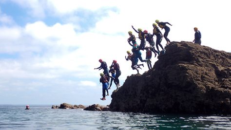 Group coasteering jump into the sea at Praa Sands during a guided session