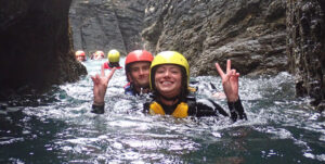 Two smiling coasteering participants in a gulley on the Cornish coast.