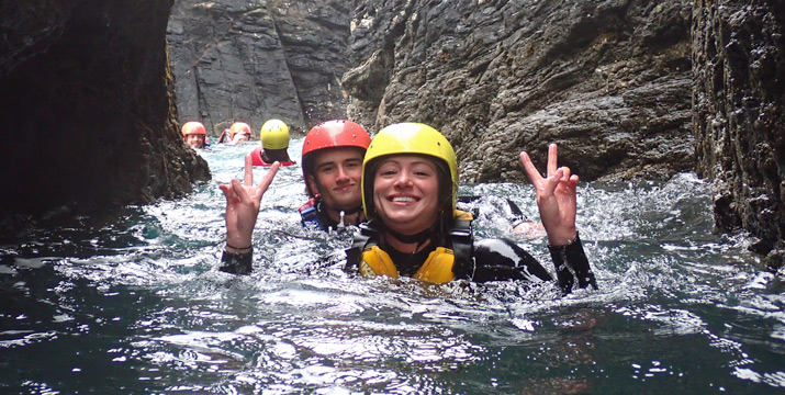Two smiling coasteering participants in a gulley on the Cornish coast.