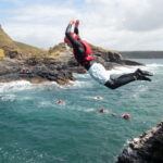 Coasteering participant jumping from a rock stack into the sea.