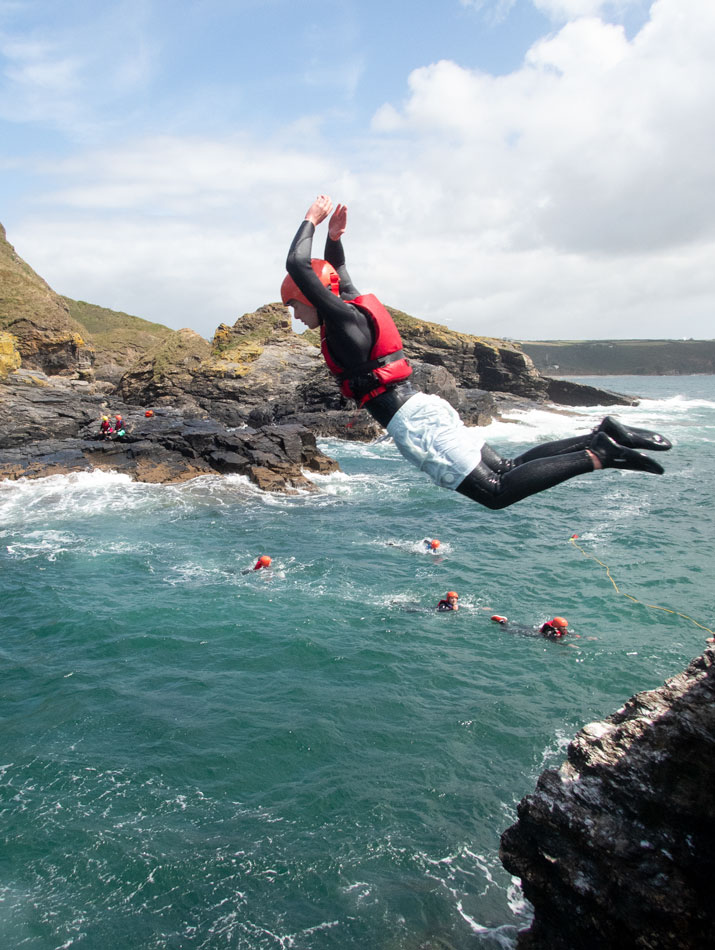 Coasteering participant jumping from a rock stack into the sea.
