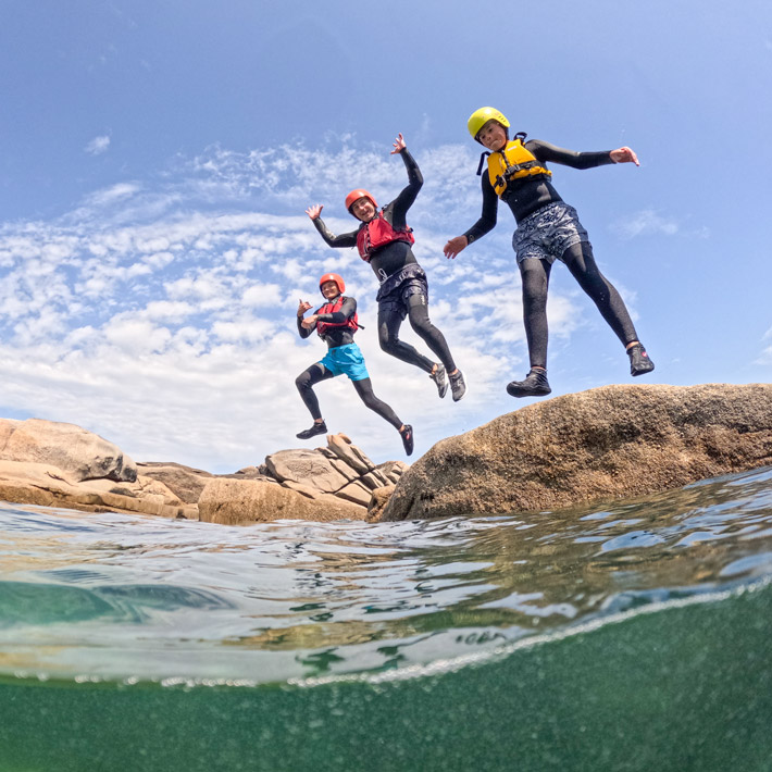 Group of three people jumping into the sea while coasteering on the Cornish coast – one of the most fun outdoor adventures and top things to do Cornwall