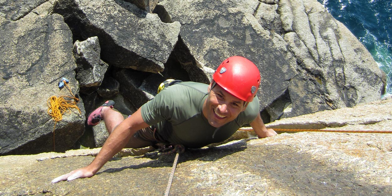 Person climbing granite cliffs above the sea on a guided Cornwall experience day – perfect for those seeking exciting things to do near Falmouth and explore new places to go in Cornwall