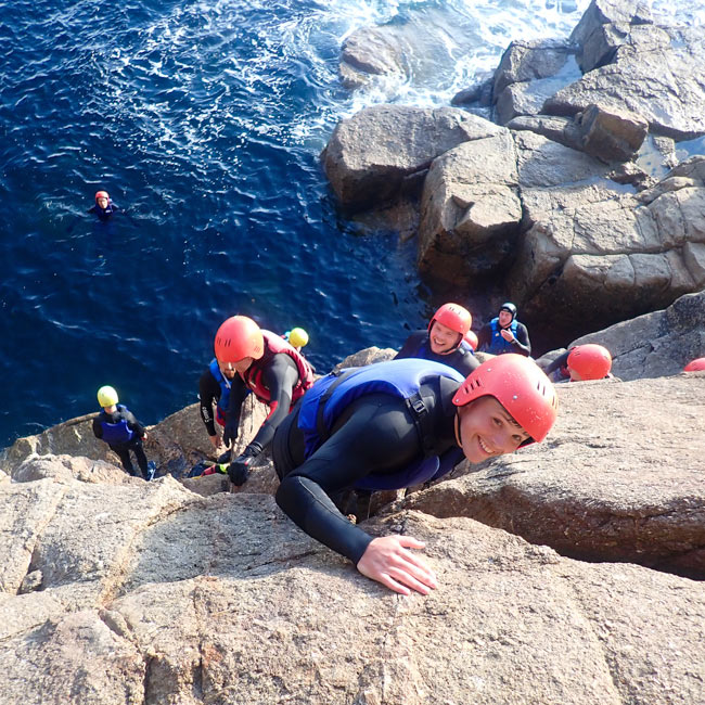 Coasteering group climbing granite ledges above Atlantic surf at Land’s End