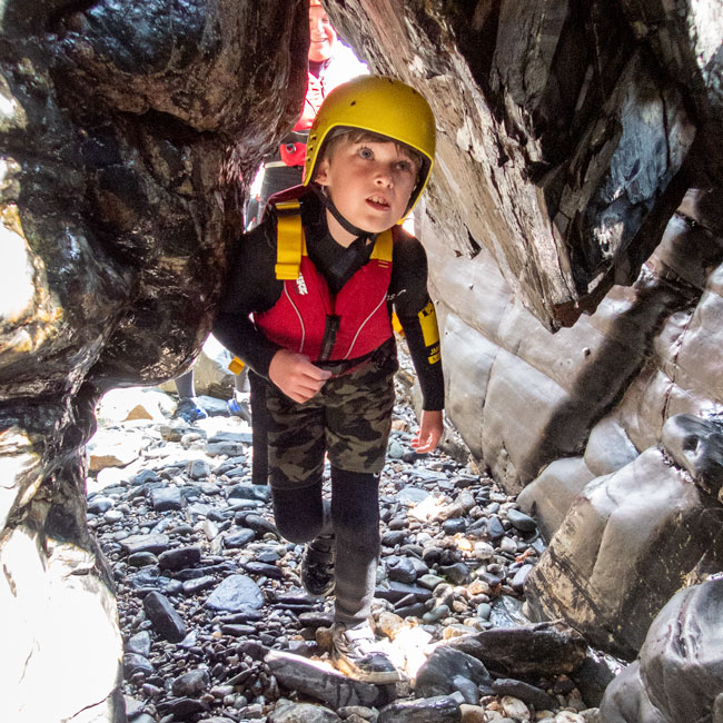 Young boy in a helmet explores a narrow sea cave — a fun and curious family activity in Cornwall.