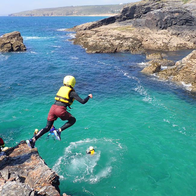 Child jumps into turquoise sea while a guide and group look on — one of the best things to do with kids in Cornwall.