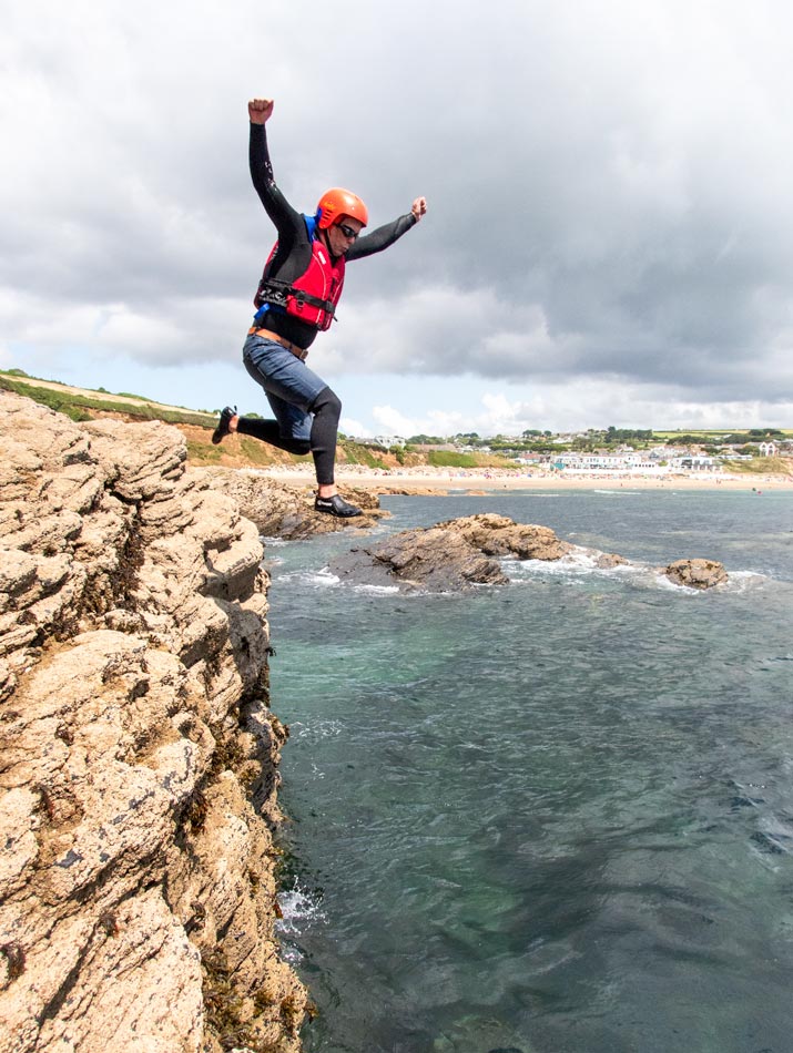 First-time coasteer leaps from a low cliff with Praa Sands beach in the distance