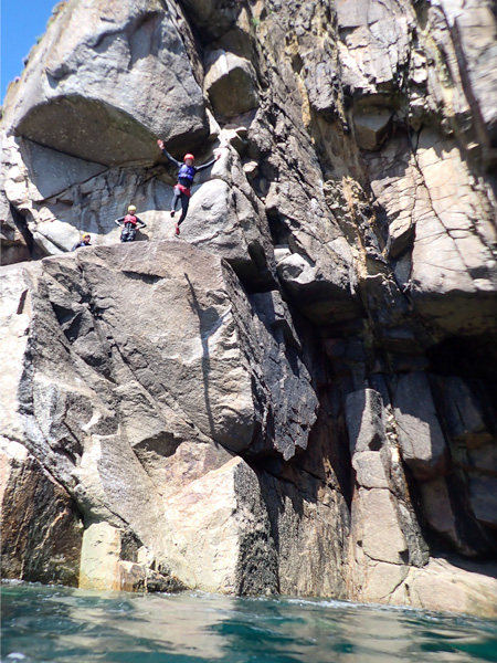 Advanced coasteering group jumping beside a massive granite sea cave at Land’s End, Cornwall