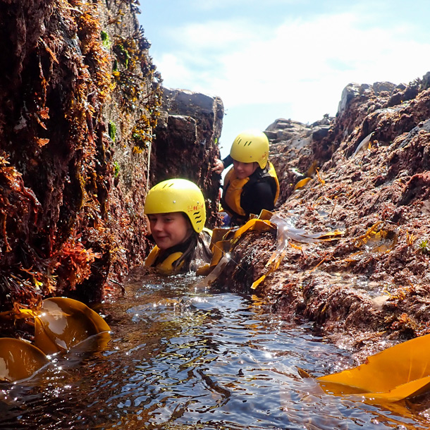 Two children making their way through a narrow seaweed-lined channel on a coastal family trip